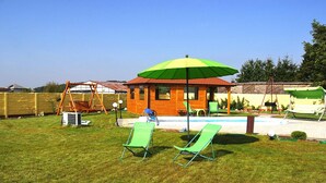 Un patio trasero con una casita de juegos de madera, un columpio, una piscina y dos sillas de jardín verdes.