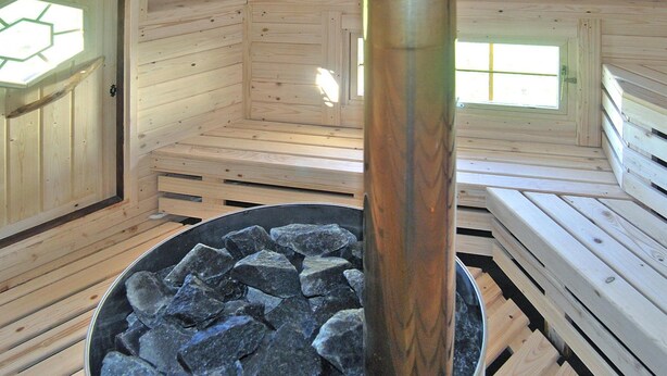 Una sauna con bancos de madera, un calentador central de piedra y un tragaluz.