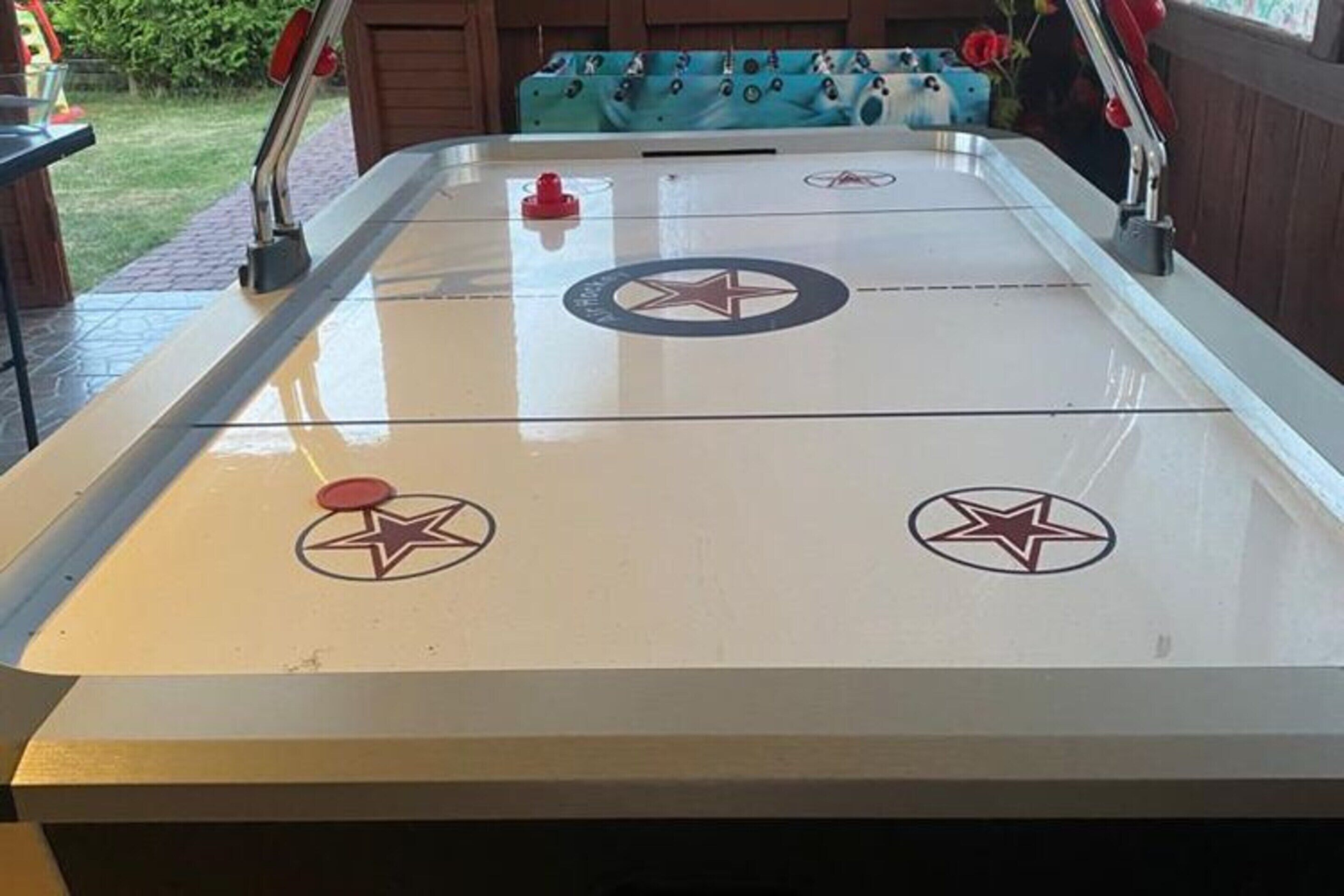A foosball table with two goal areas marked by stars, surrounded by a wooden table with a blue cushioned bench.