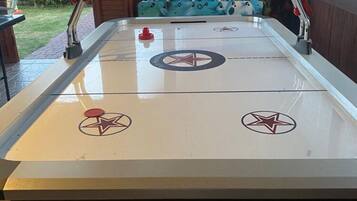 A foosball table with two goal areas marked by stars, surrounded by a wooden table with a blue cushioned bench.