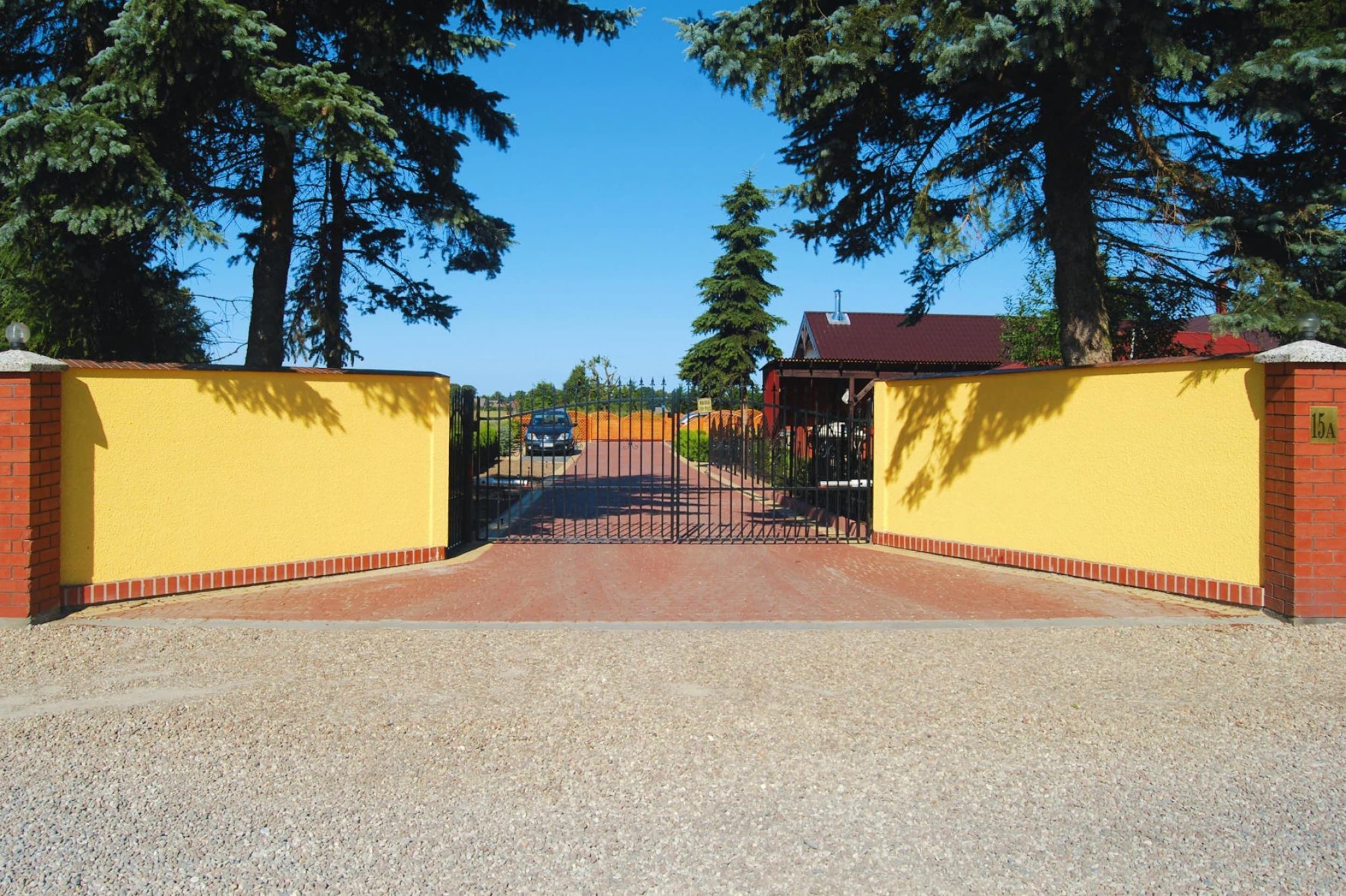 A gated entrance with a yellow wall, a brick base, and a metal gate.