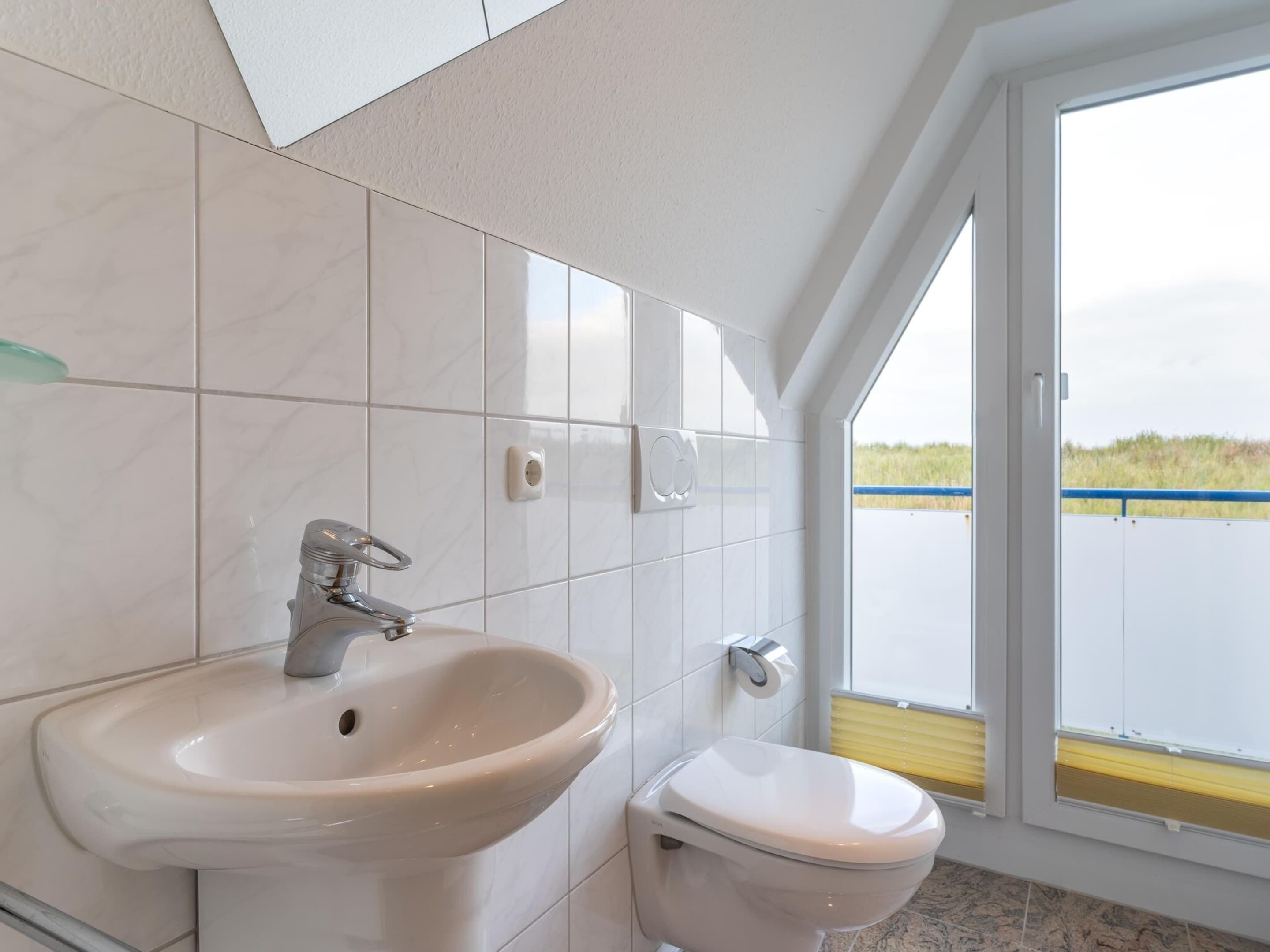 A bathroom with a sink, toilet, and a large window offering a view of a body of water.