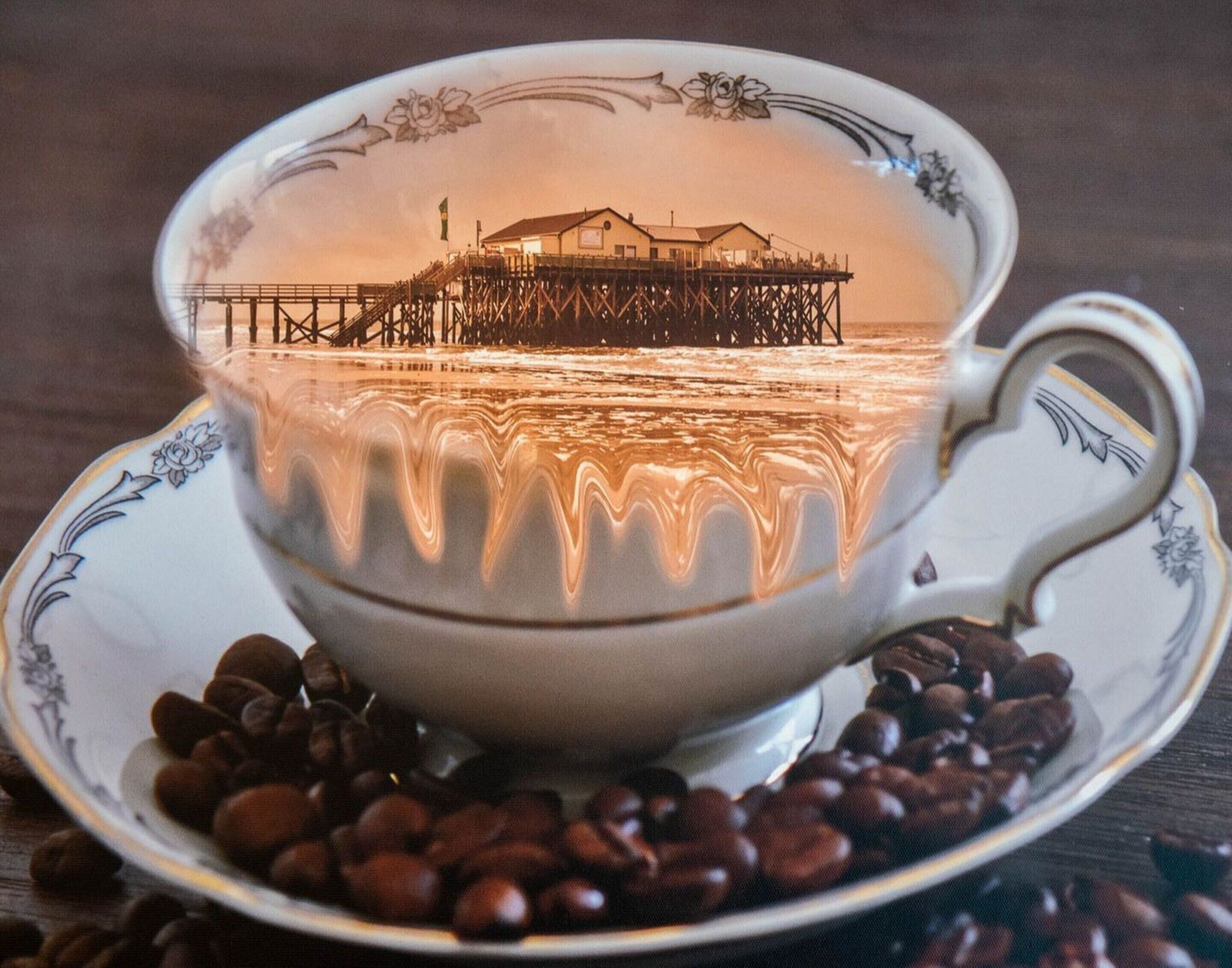 A cup of coffee with a scenic view of a pier and a building reflected on the surface.