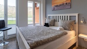 A bedroom with a large bed, a chair, a painting, and a view of the outdoors. - Comfortable Holiday Apartment in St. Peter Ording (St. Peter-Ording)