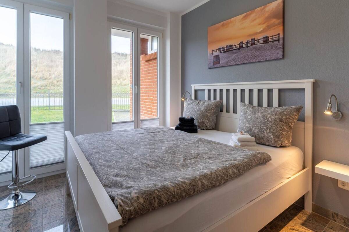 Une chambre avec un grand lit, une chaise, un tableau et une vue sur l’extérieur.