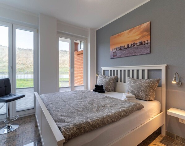 A bedroom with a large bed, a chair, a painting, and a view of the outdoors. - Comfortable Holiday Apartment in St. Peter Ording (St. Peter-Ording)