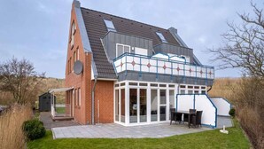 A modern house with a sloped roof, large windows, and a covered patio area. - Comfortable Holiday Apartment in St. Peter Ording (St. Peter-Ording)