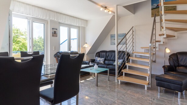 A modern living room with a black leather sofa, a glass coffee table, and a staircase with wooden steps. - Comfortable Holiday Apartment in St. Peter Ording (St. Peter-Ording)