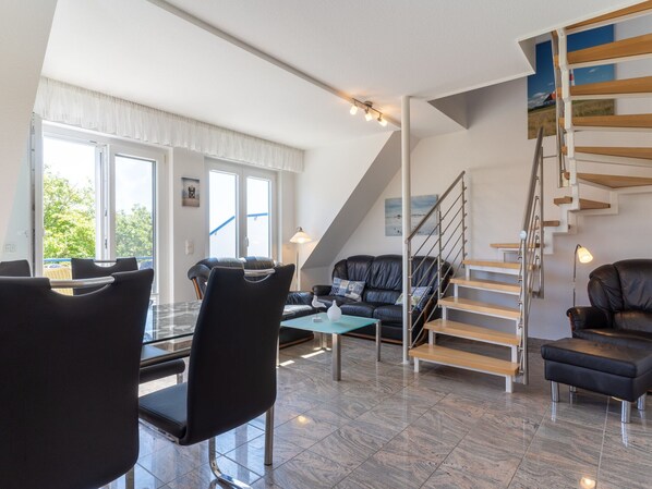 A modern living room with a black leather sofa, a glass coffee table, and a staircase with wooden steps. - Comfortable Holiday Apartment in St. Peter Ording (St. Peter-Ording)