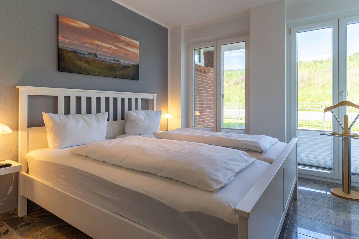 Une chambre avec deux lits, un tableau au mur et une vue sur la verdure par la fenêtre.