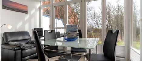 A modern living room with a glass table, black leather chairs, a black leather sofa, and a large window with a view of trees and a building.