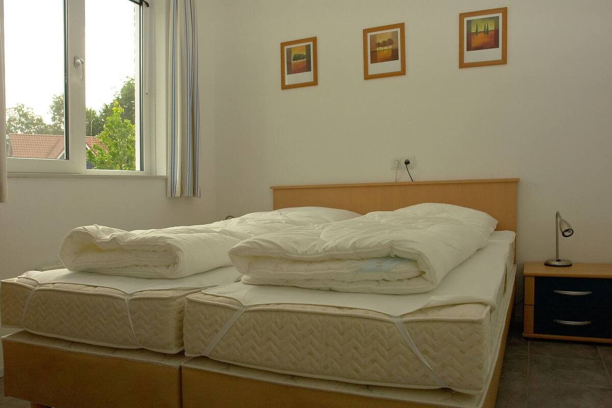 A neatly made bed with a wooden headboard, a bedside table with a lamp, and three framed pictures on the wall.