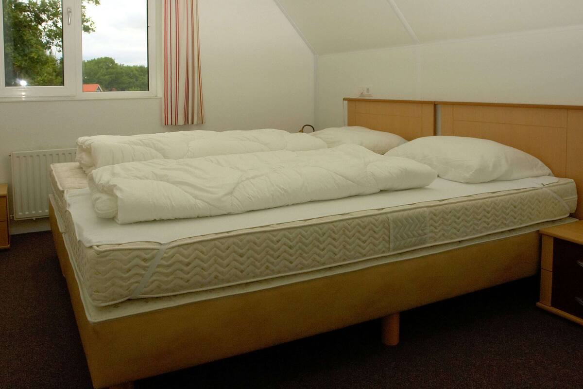 A single bed with a wooden headboard and footboard, a white mattress, and a neatly folded white blanket.