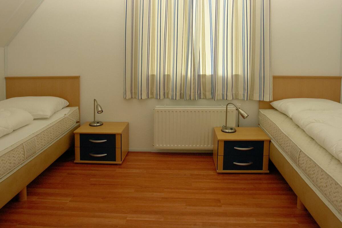 A bedroom with two single beds, wooden nightstands, and a radiator.