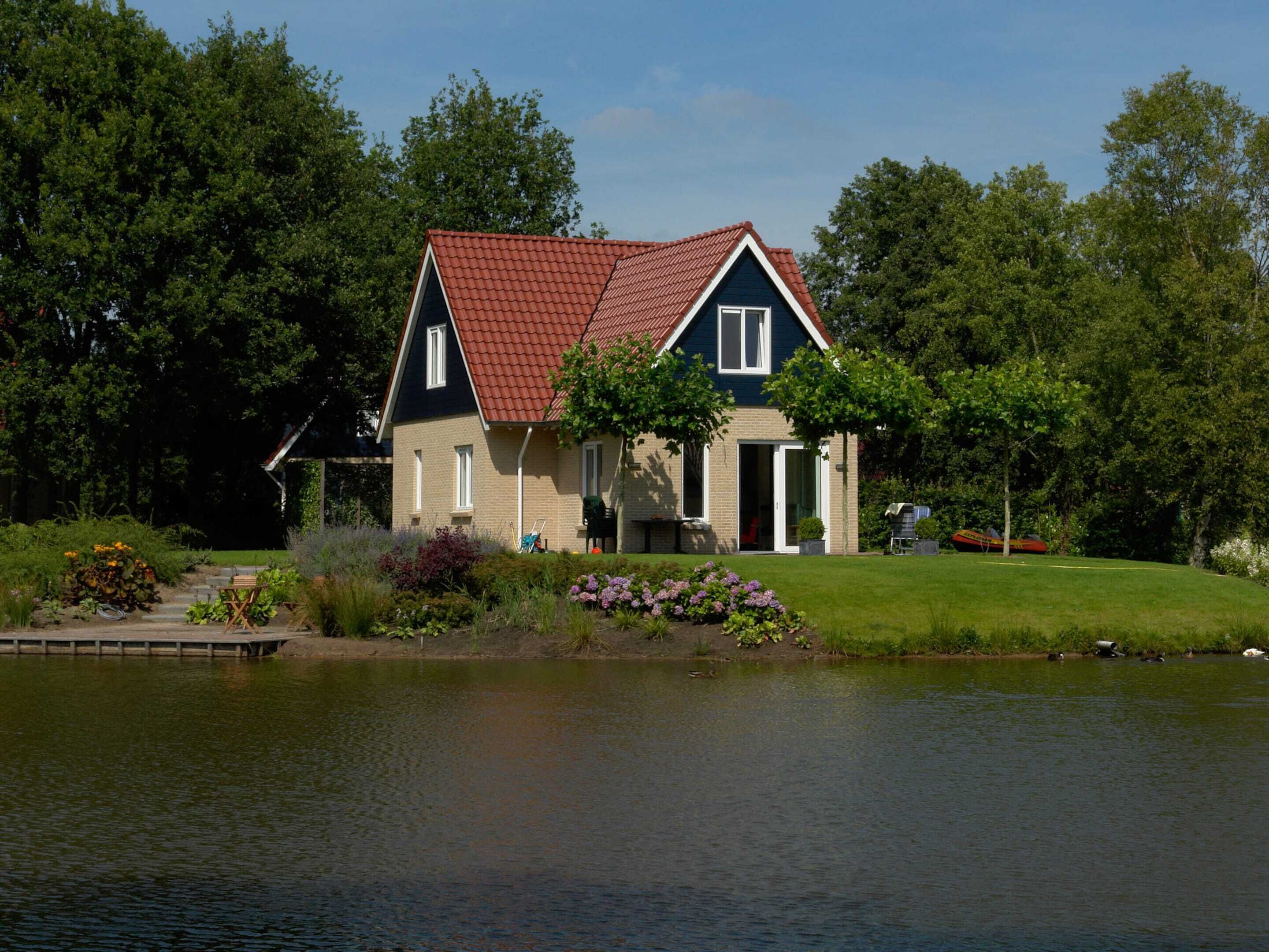 Een huis met een rood dak, een donkerblauwe gevel en een kleine tuin met paarse bloemen.