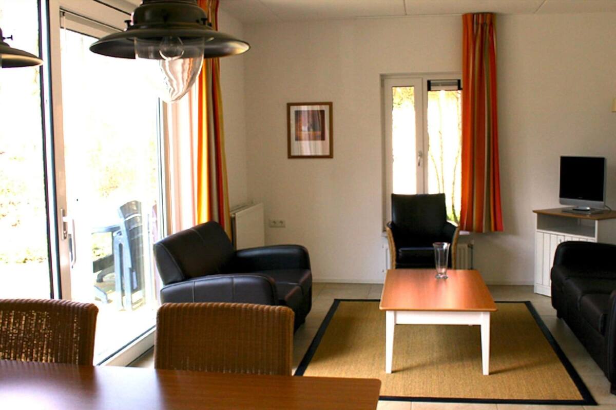 A living room with a sofa, armchair, and a coffee table. There is a television on a stand to the right.