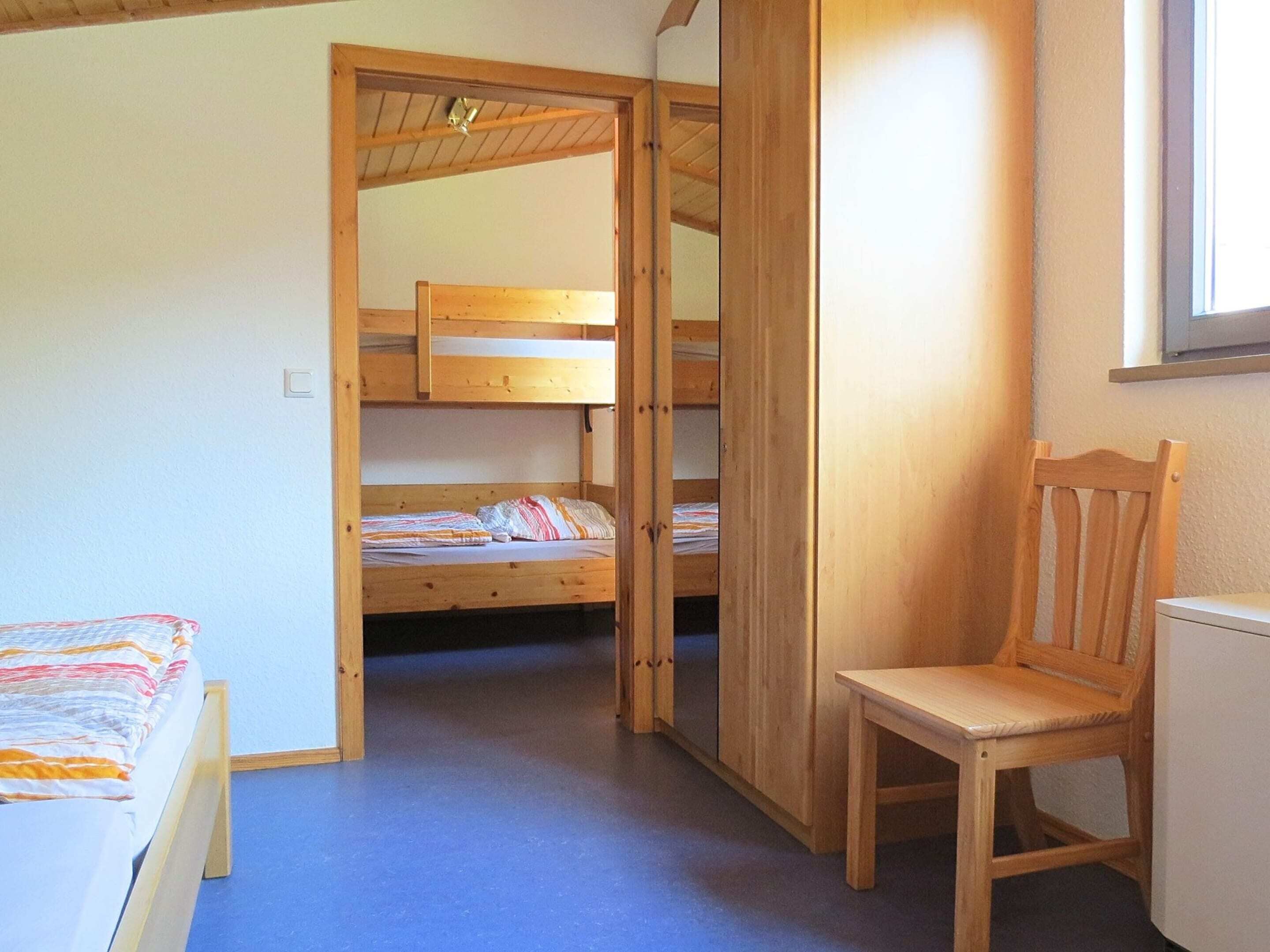 Una habitación con literas, una silla de madera y un ventanal.