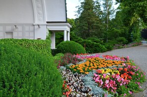 A white building with a covered porch, surrounded by lush greenery and a colorful flower bed. - Holiday Farm Situated Next to the Kellerwald-edersee National Park With a Sunbathing Lawn (Bad Wildungen)