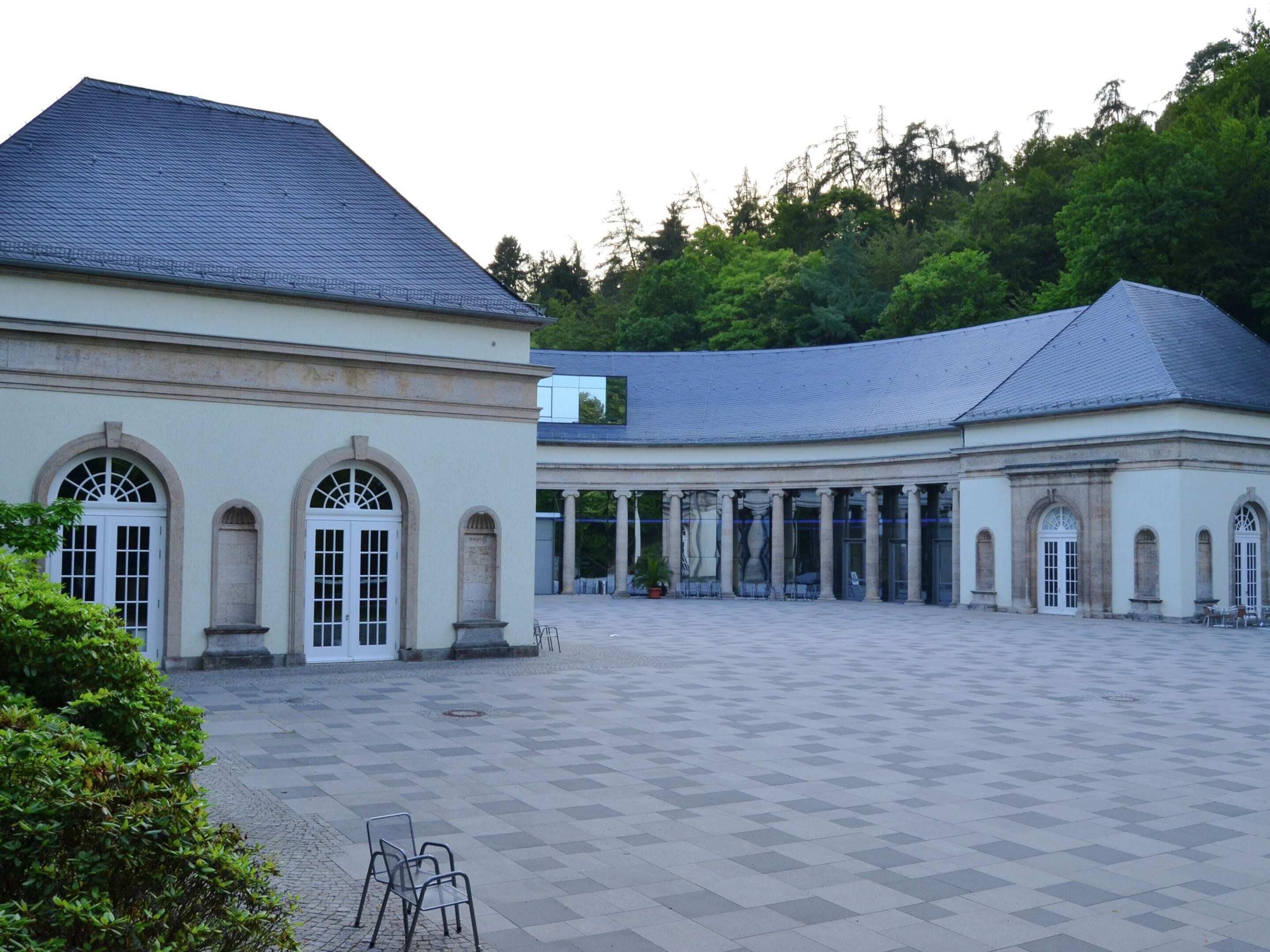 Ein weitläufiger Innenhof mit einem klassizistischen Gebäude, das Rundbogenfenster und Säulen aufweist.