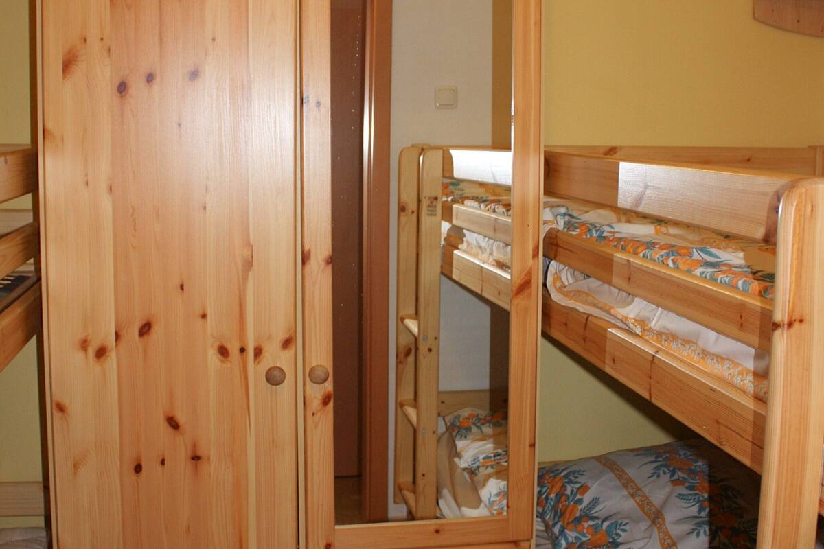 Ein hölzernes Etagenbett mit einem unteren und einem oberen Bett, beide mit Blumenmuster-Bettwäsche.
