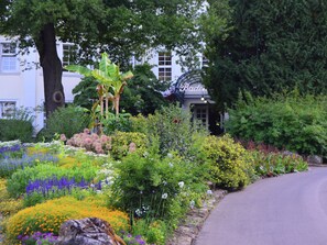 En have med mange blomster og planter, en stensti og en bygning med skiltet "Baden".