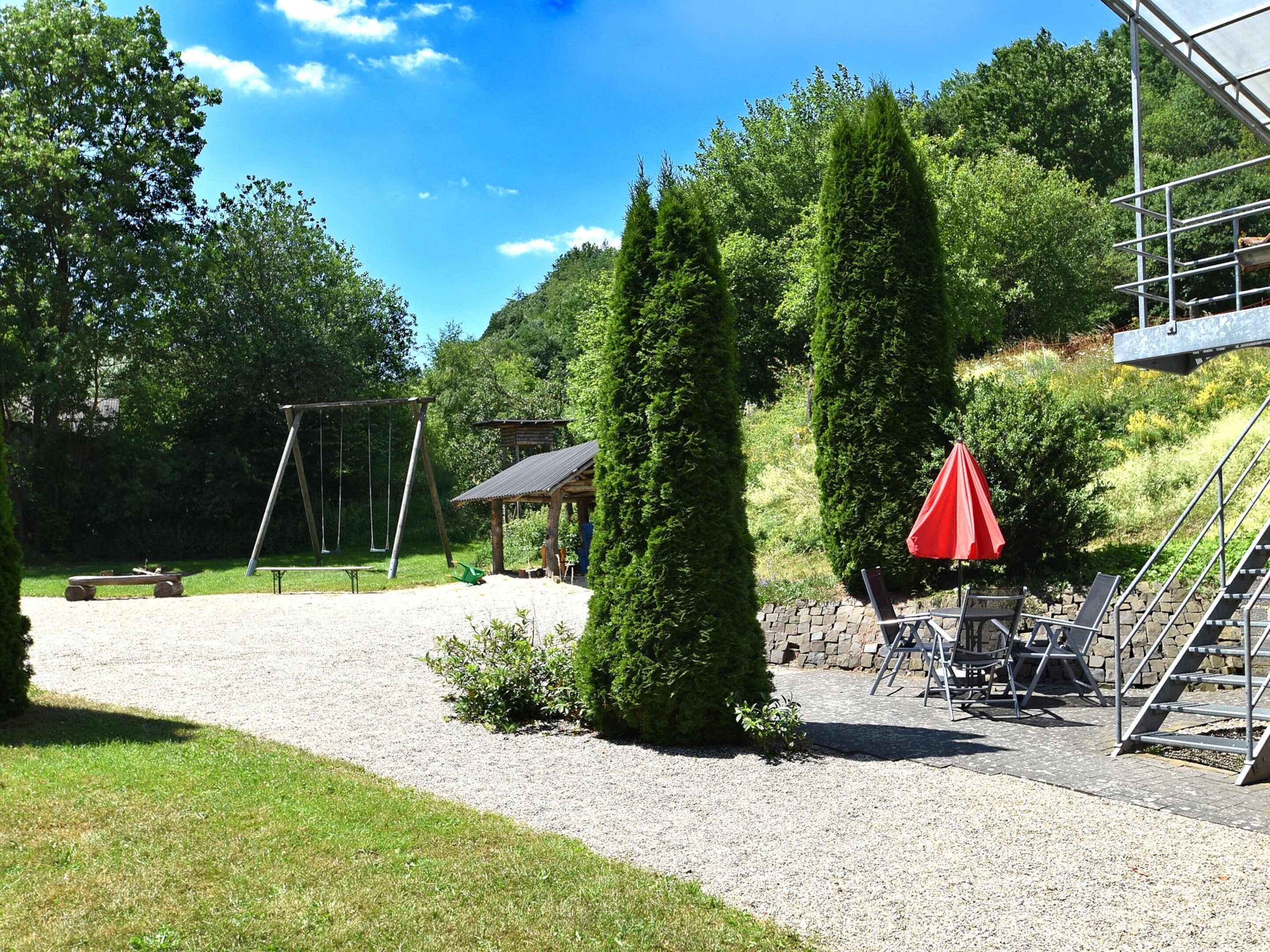 Um parque com baloiço, um coreto e um guarda-sol vermelho.