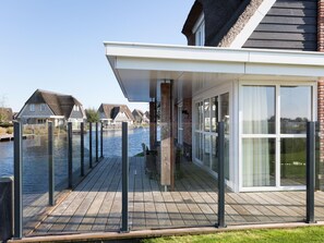 Une maison moderne dotée d’une terrasse donnant sur un canal, avec de grandes fenêtres et une façade en briques.