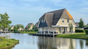 Une maison avec un toit de chaume, un quai et une étendue d’eau calme devant.