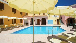 Area piscina con numerosi ombrelloni gialli, sdraio e una piscina azzurra e limpida.