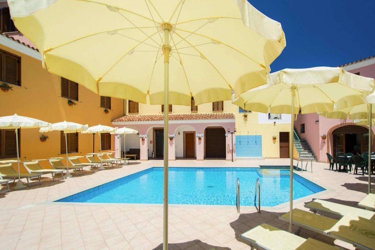 Un espace piscine agrémenté de plusieurs parasols jaunes, de chaises longues et d’une piscine à l’eau d’un bleu limpide.
