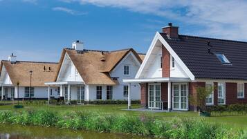 A row of houses with thatched roofs and a pond in the foreground.