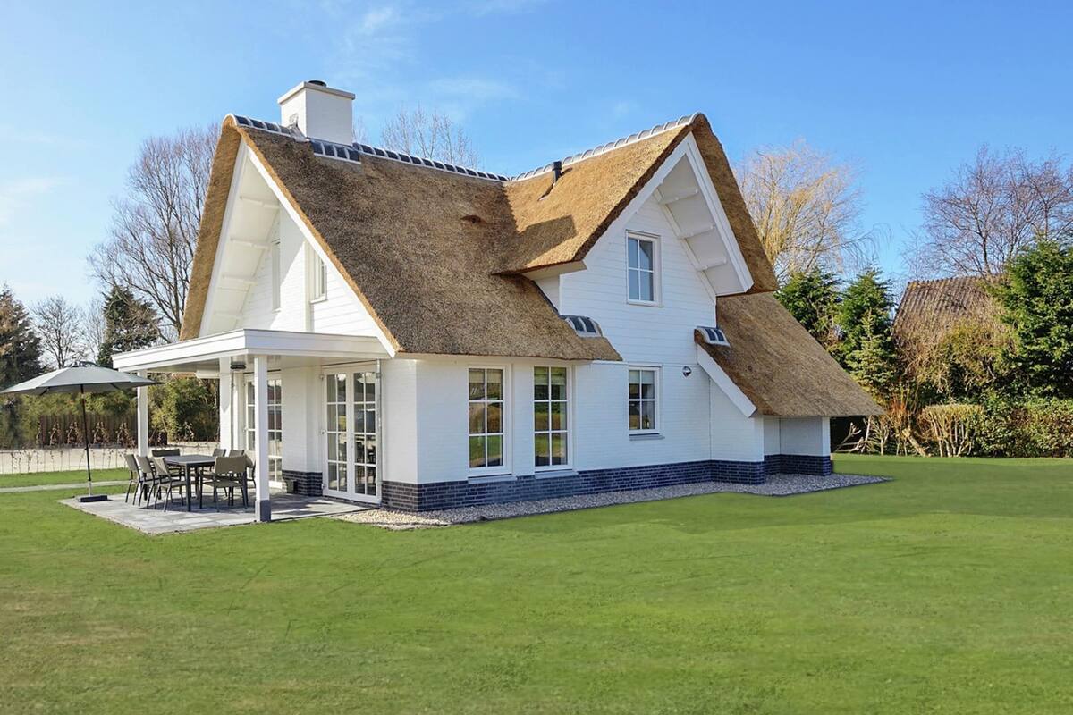 A large house with a thatched roof, white exterior walls, and a covered patio with outdoor furniture.