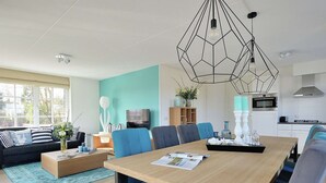 A modern living room with a dining area, featuring a wooden table, blue chairs, and a geometric pendant light. - Beautiful Villa With Lots of Comfort, Near North Sea Beach (Noordwijk)