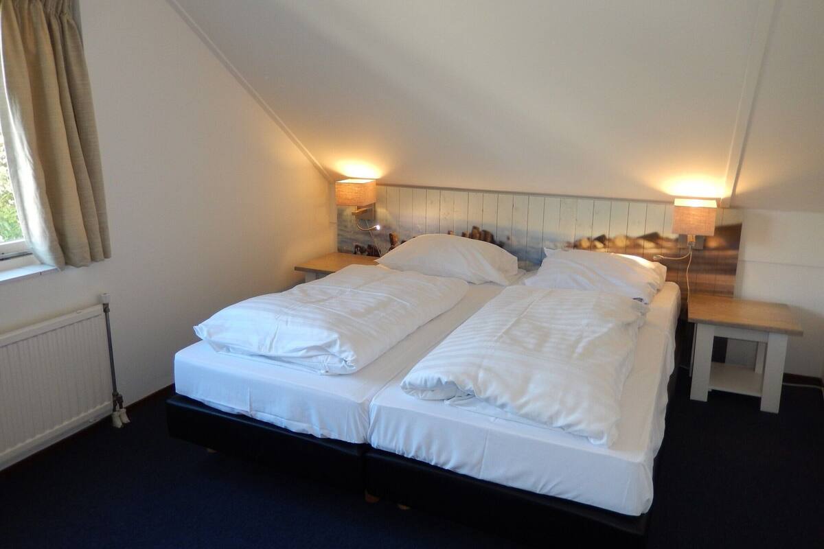 A bedroom with a bed, two bedside tables, and a window with curtains.