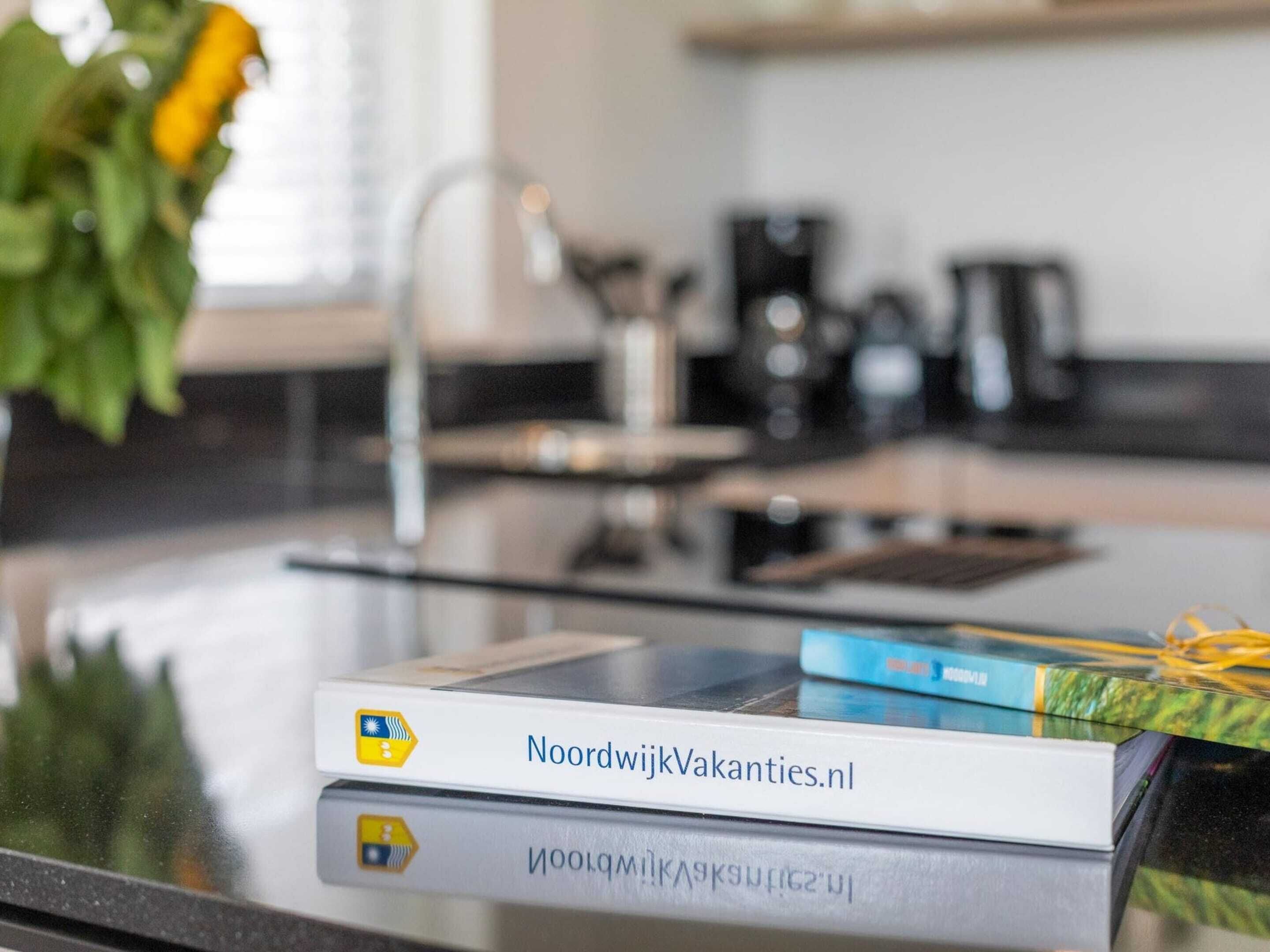 Una encimera de cocina con una cafetera, un hervidor y un libro titulado 'NoordwijkVakanties.nl'.