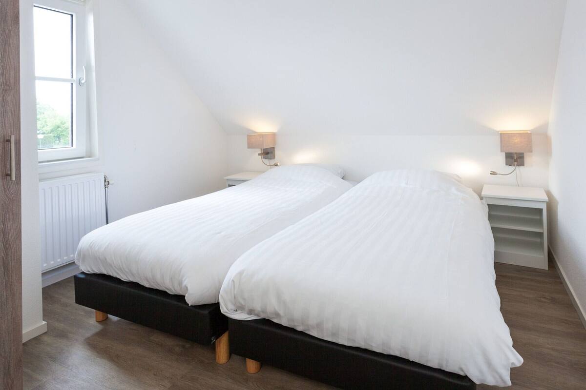 A bedroom with two beds, a window, and bedside lamps.