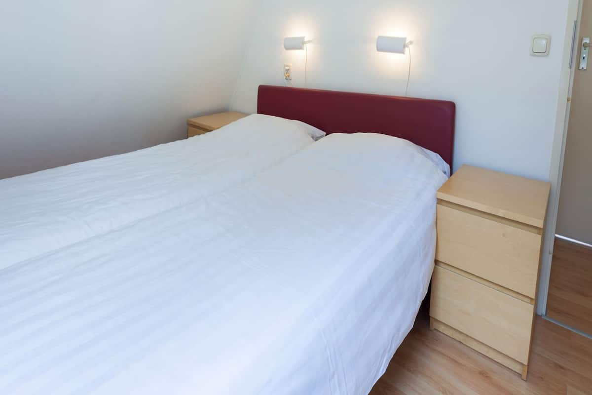 A neatly made bed with white bedding, a red headboard, and two bedside tables with light fixtures.