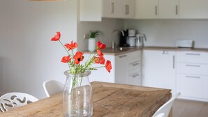 A wooden table with a clear glass vase containing red flowers. White chairs are around the table. - Lovely Apartment on Ameland Near Nes (Nes)