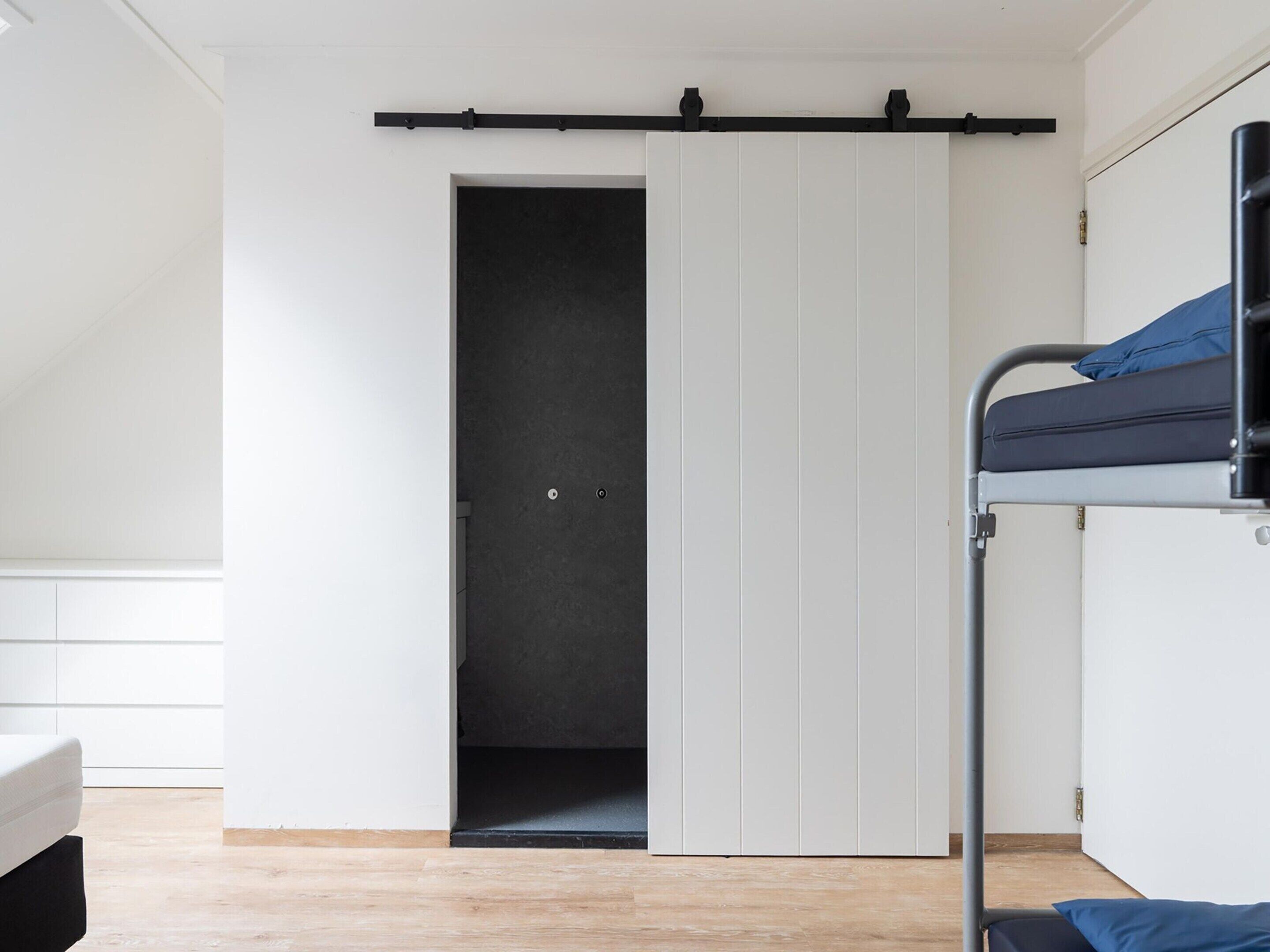 A room with a bunk bed, a sliding door, and a white wardrobe.