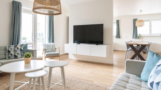 A modern living room with a sofa, a dining table, and a TV on a white cabinet. - Lovely Apartment on Ameland Near Nes (Nes)