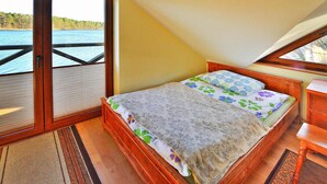 A bedroom with a wooden bed, a view of a lake through a sliding door, and a small wooden nightstand. - Holiday House by the Lake With a Fireplace (gmina Manowo)