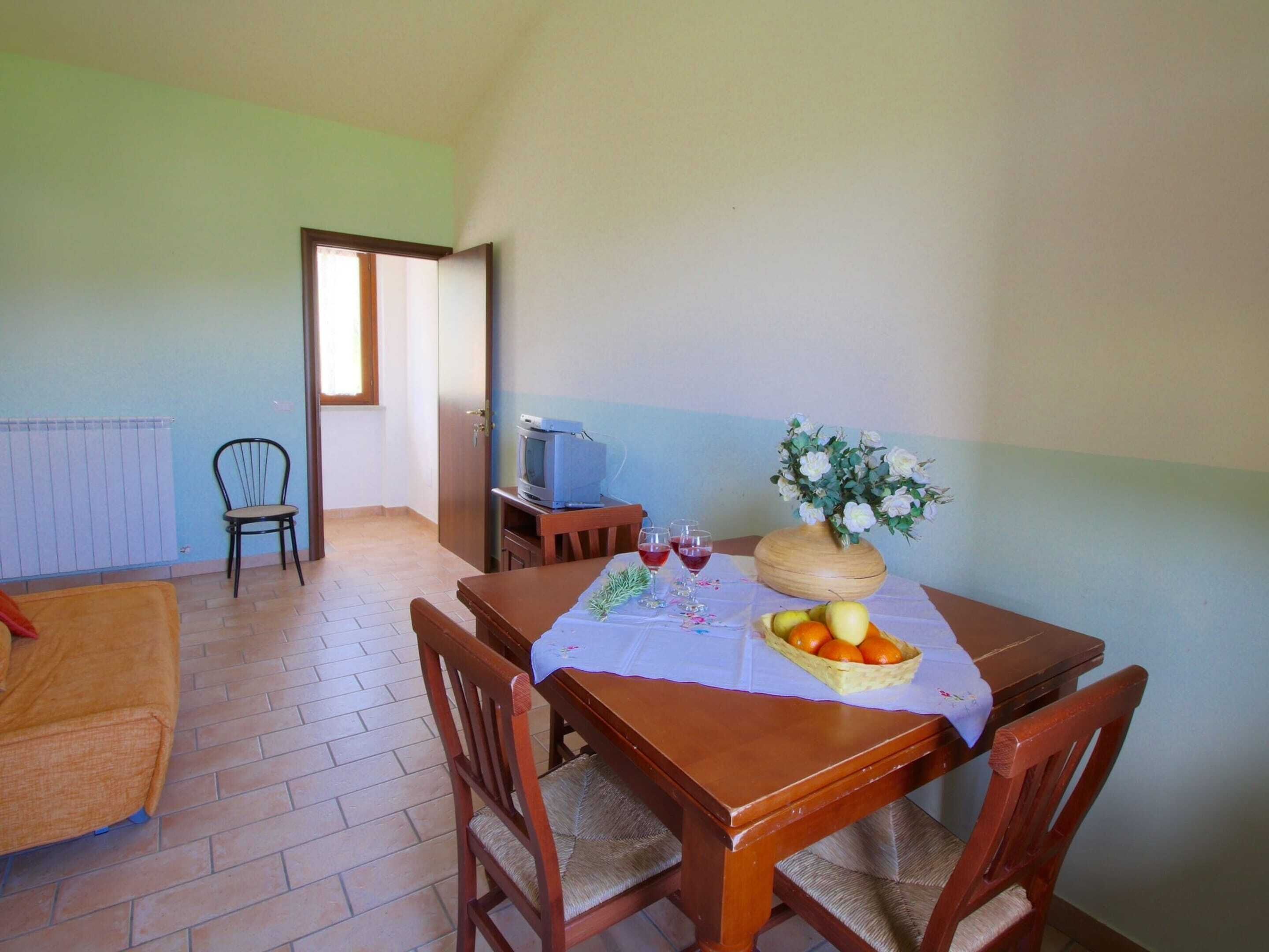A dining area with a table set for two, a television, and a vase of flowers.