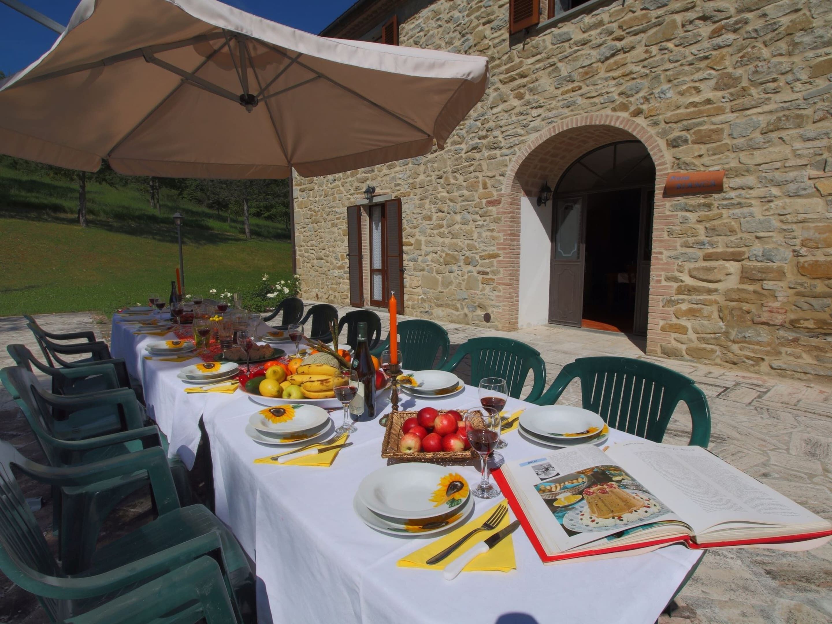 An outdoor dining setup with a stone building in the background, a table set with plates, glasses, and a book.