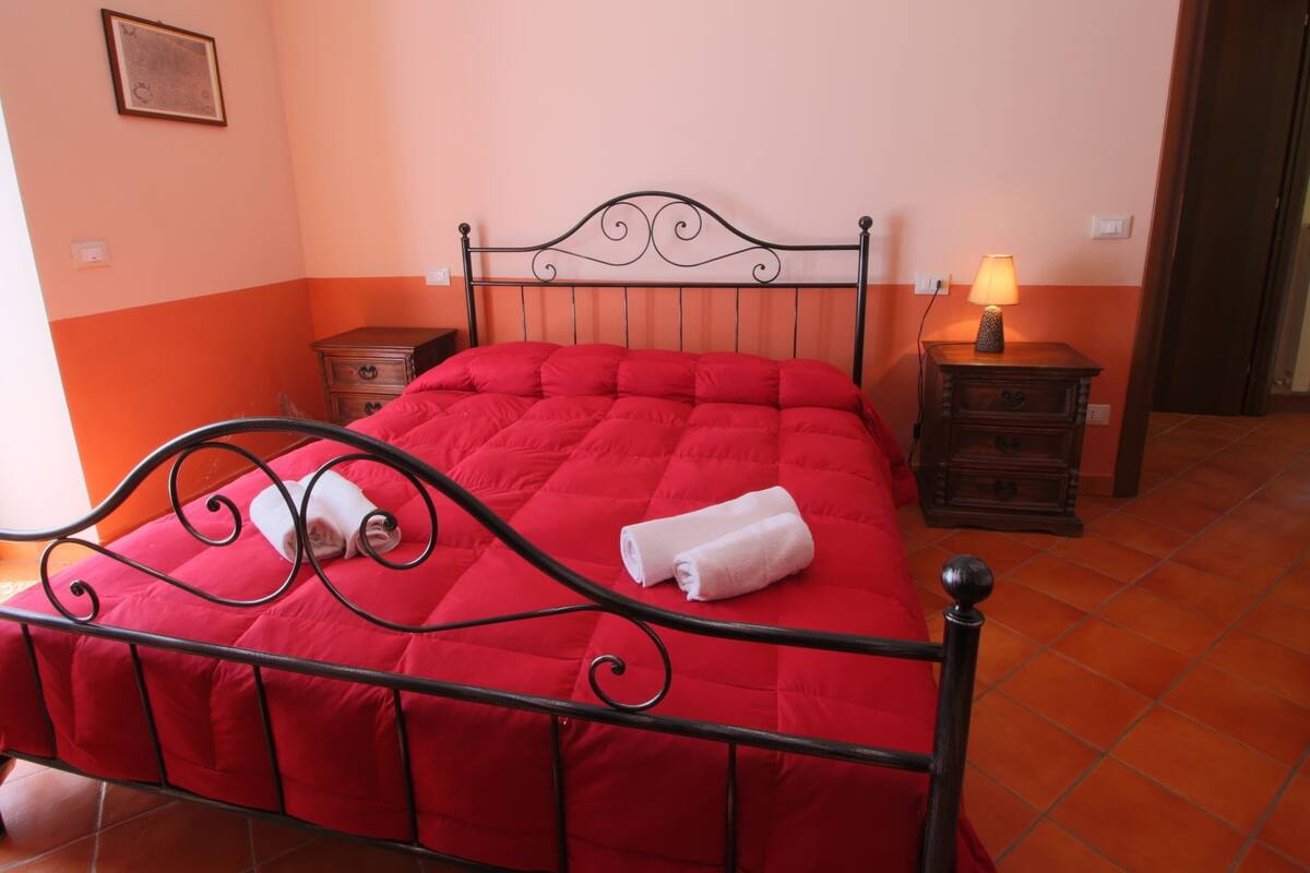 A room with a red bed, a nightstand with a lamp, and a wooden dresser.