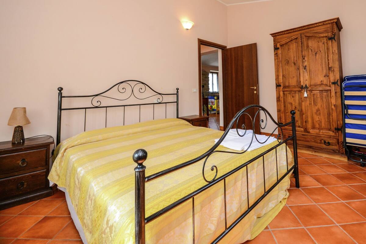 A bedroom with a bed, a wooden wardrobe, a nightstand, and a lamp.