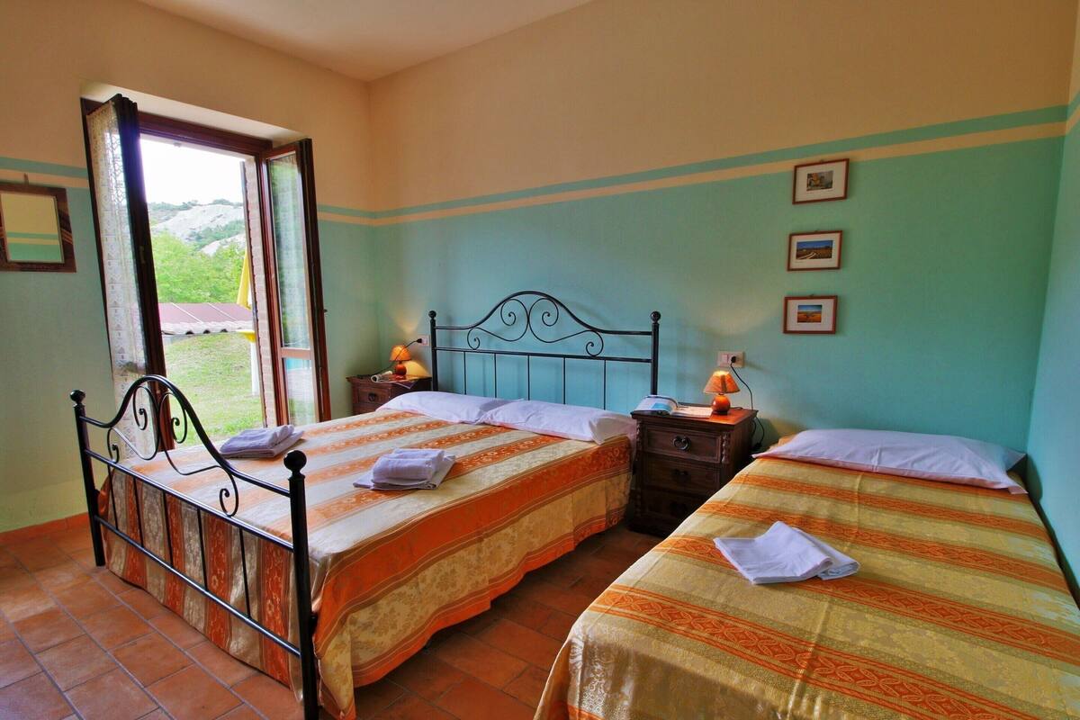 A room with two beds, a window, and a nightstand with a lamp.