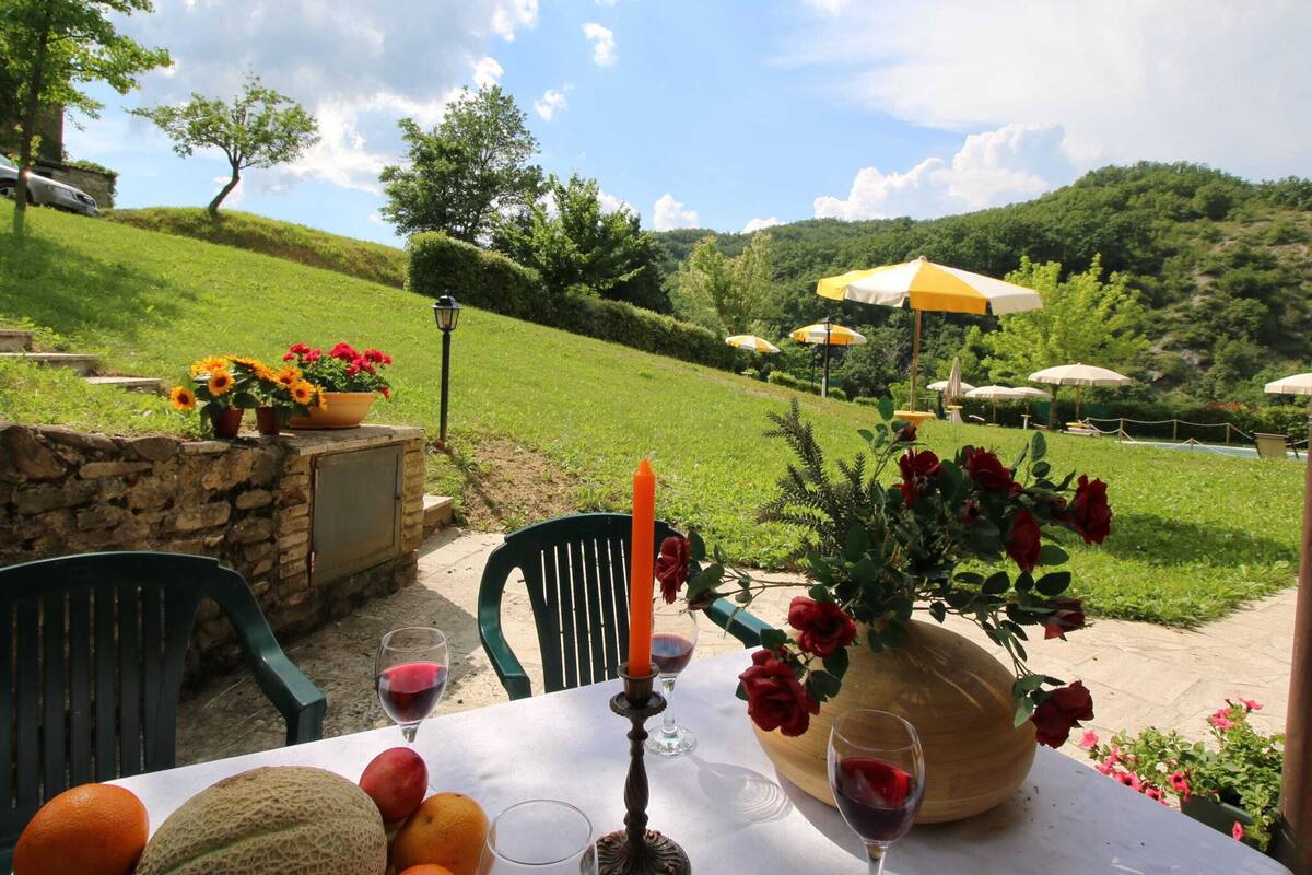 A table set outdoors with a view of a hillside, a stone wall, and umbrellas.