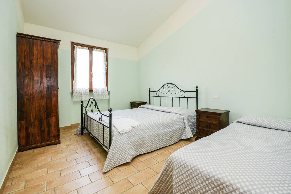 A bedroom with two beds, a wooden wardrobe, and a window with lace curtains.