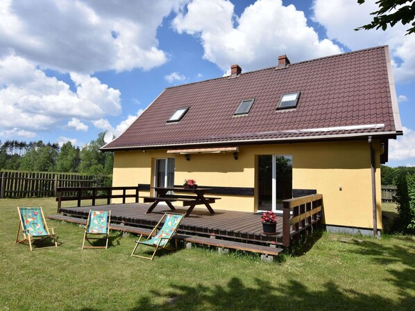 A yellow house with a tiled roof, a wooden deck, and a picnic table. - Cottage in a Quiet Location by the Lake Mausz, Parchowo in Kashubia (Parchowo)