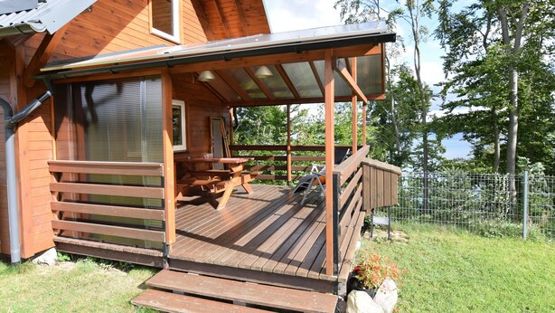 Une cabane en bois dotée d’une terrasse couverte, d’une table de pique-nique et d’une cour clôturée.